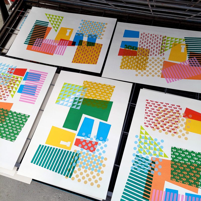 a set of screenprints on a drying rack. each print is a collection of the same motifs repeated in different combinations and colours.