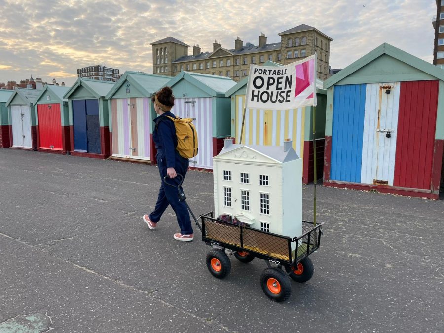 A collage of 4 images. 2 interior scenes of a dolls house decorated with custom miniature art. One image of Artist pulling her house along the seafront on a cart and one of the artist’s head looming through a connecting door in the dolls house, a mini paintbrush in her mouth.