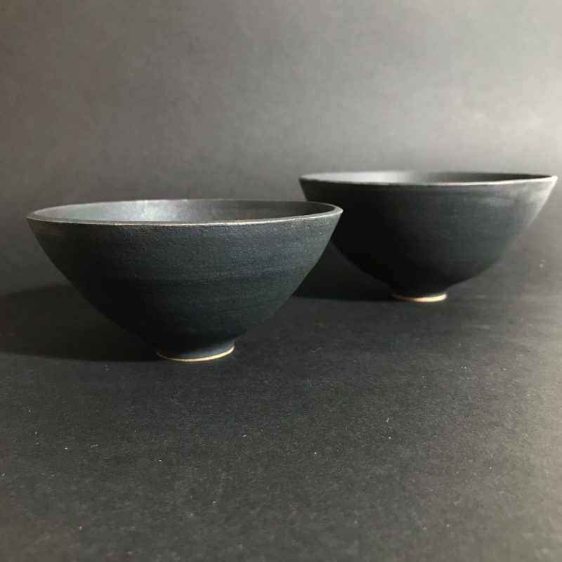 two black clay oxide glazed handmade ceramic bowl in front of a black background