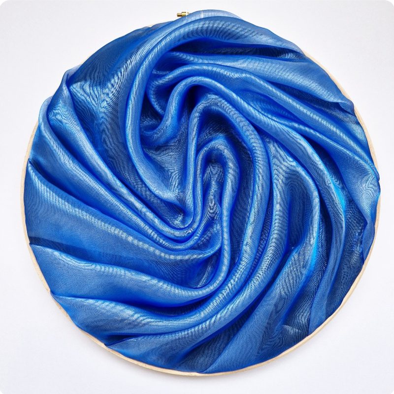 A 12in wooden embroidery hoop with sculpted royal blue organza fabric.