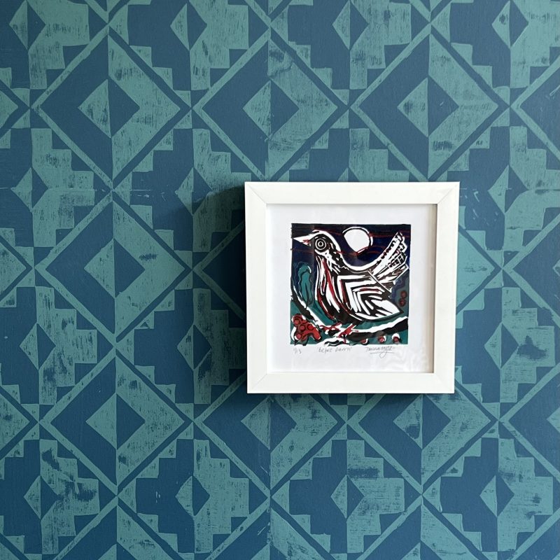Blue and green wallpaper with a bird lino print in a white frame