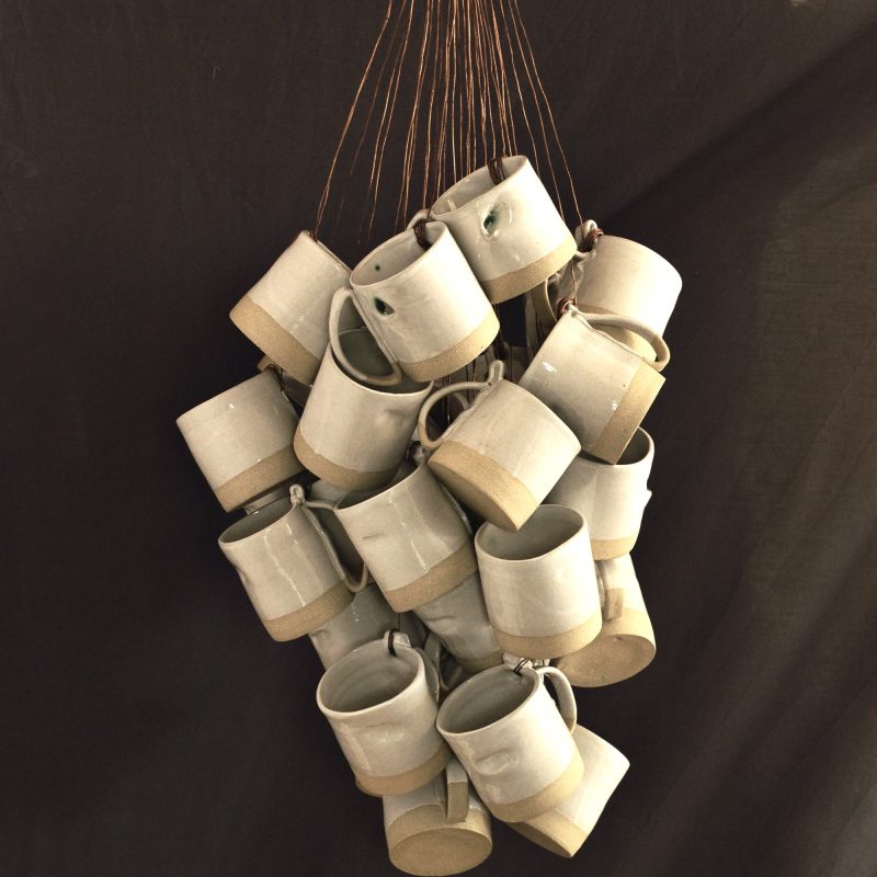 A collection of twenty pale ceramic mugs hanging on copper wire from the ceiling 