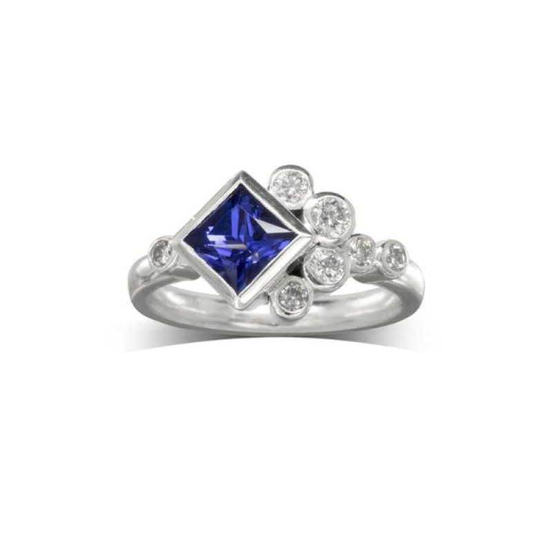 A white gold ring featuring a square blue gemstone and multiple small round diamonds arranged asymmetrically on the band.