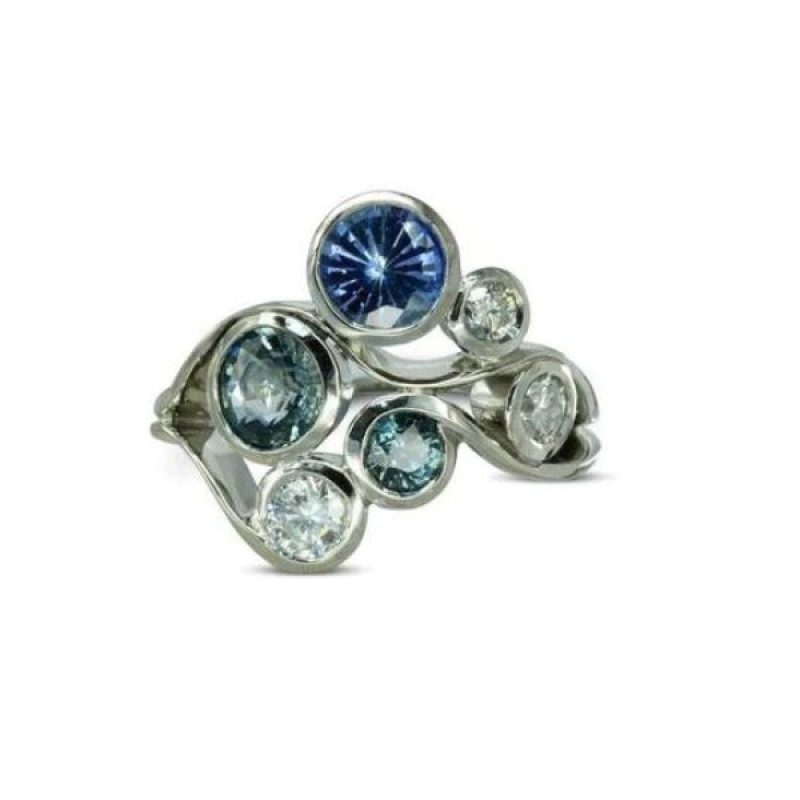 A platinum ring with round diamonds and blue sapphires in a cluster pattern with waves of metal curving between the stones