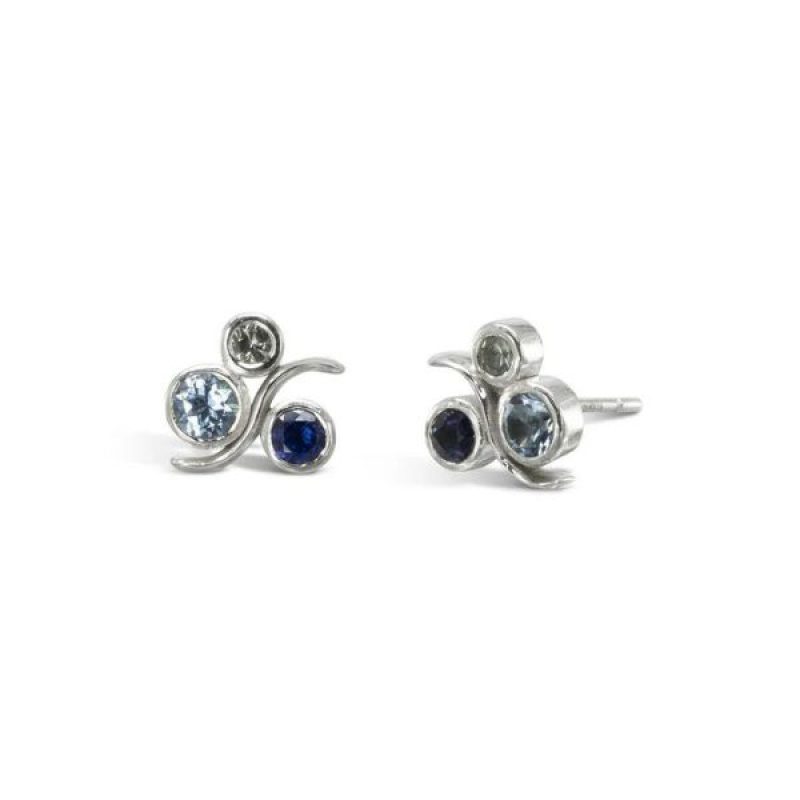 White gold earrings with a round diamond, teal sapphire, and blue sapphire with a curved gold wave crossing through them