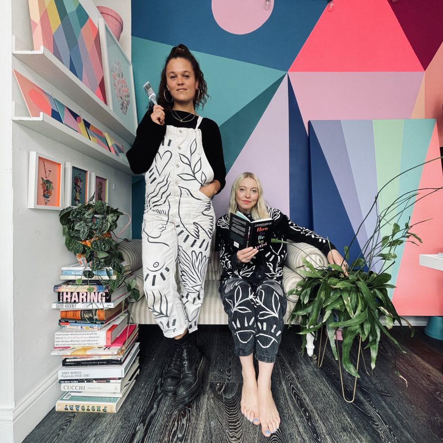 Amy and Amber in the studio wearing Amy's illustrated clothing, showcasing Amber's colourful mural.