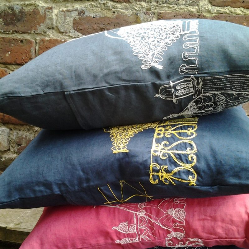 Stack of linen cushions in different colours with machine embroidery images of Brighton