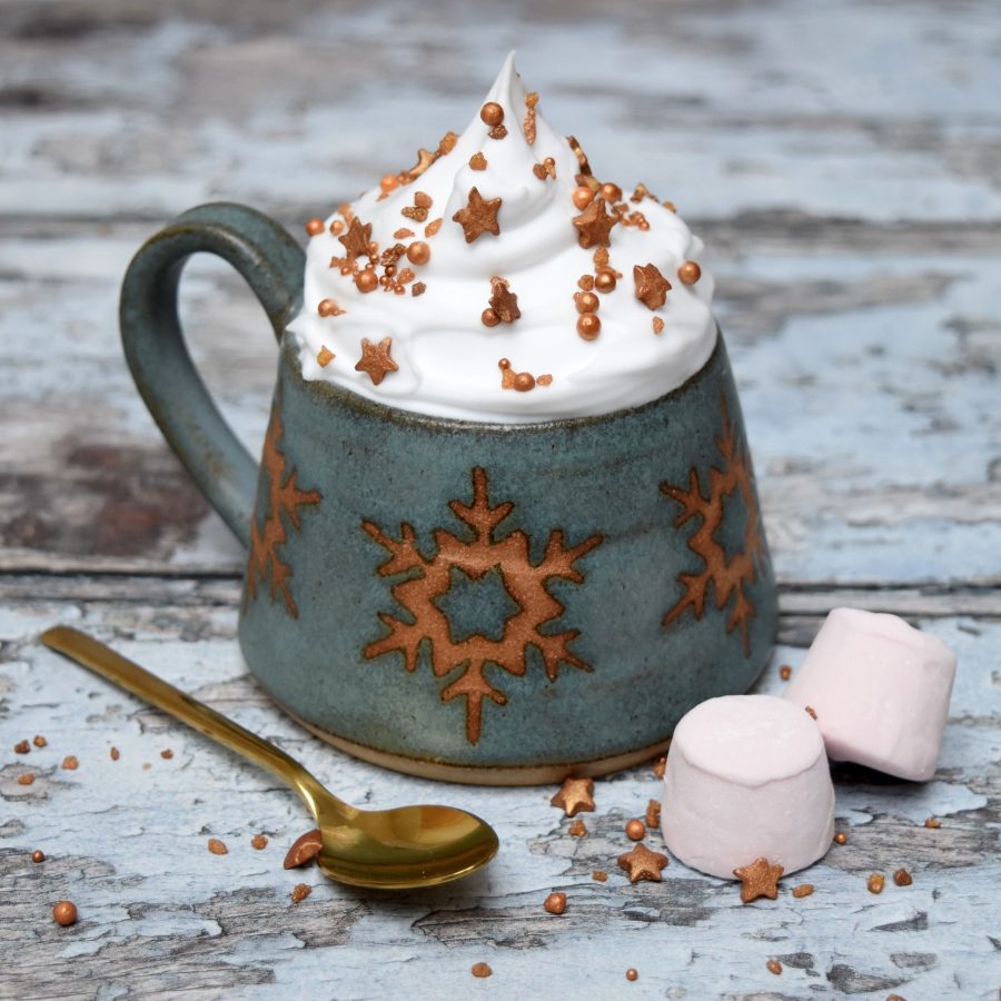 A stoneware ceramic mug with turquoise blue glaze and snowflake motif.