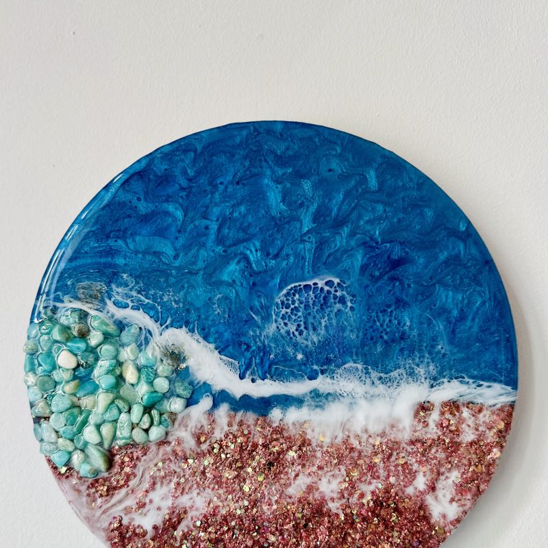 Resin seascape on 10” round wooden cradled panel. Layers of epoxy resin in beautiful shades of blue & teal create a stunning seascape finished with contrasting white sea foam detailing. As each resin painting is hand poured, it is truly one of a kind.