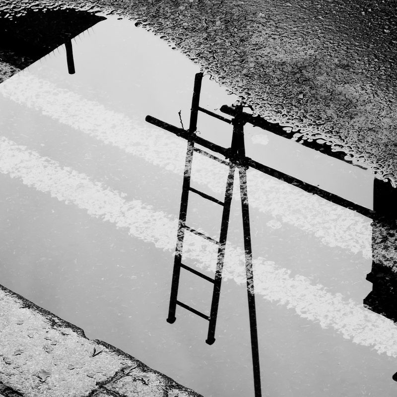 Ladder and scaffolding reflected in large puddle at the side of the road. Black and white image