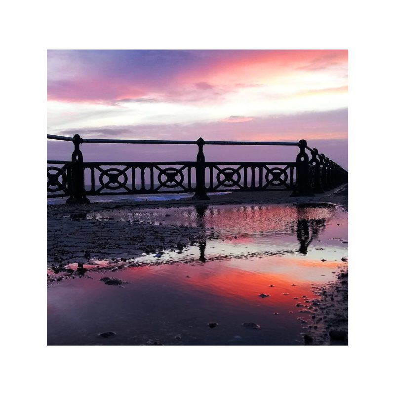 Sunset seen through seafront railings and reflections in pool of water