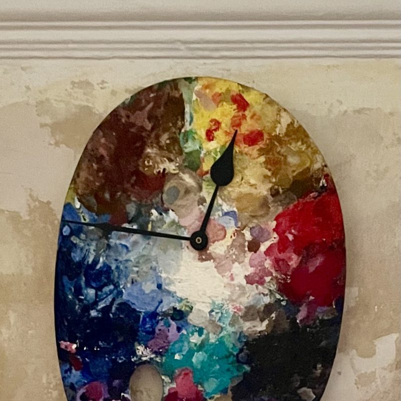 an old painter's palette made into a clock with an old paint brush for pendulum