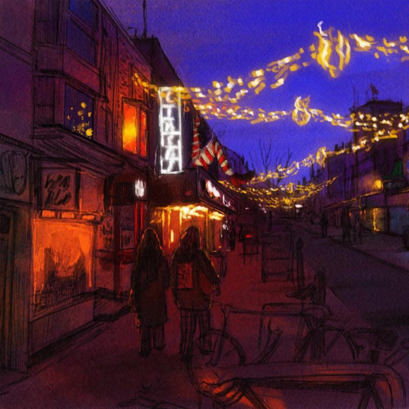 Night time painting of Gardner Street in Brighton at Christmas time, with a view of Komedia. The scene is lit by warm shop lights and festive string lights hanging overhead.