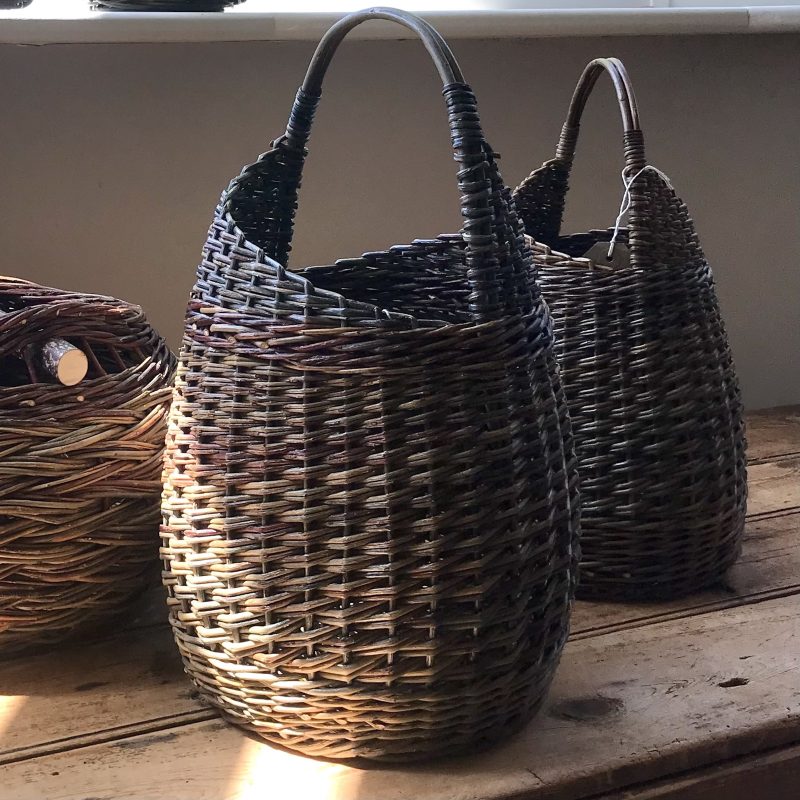 A small woven basket made with fine colourful willow rods, with a sloping top and handle.