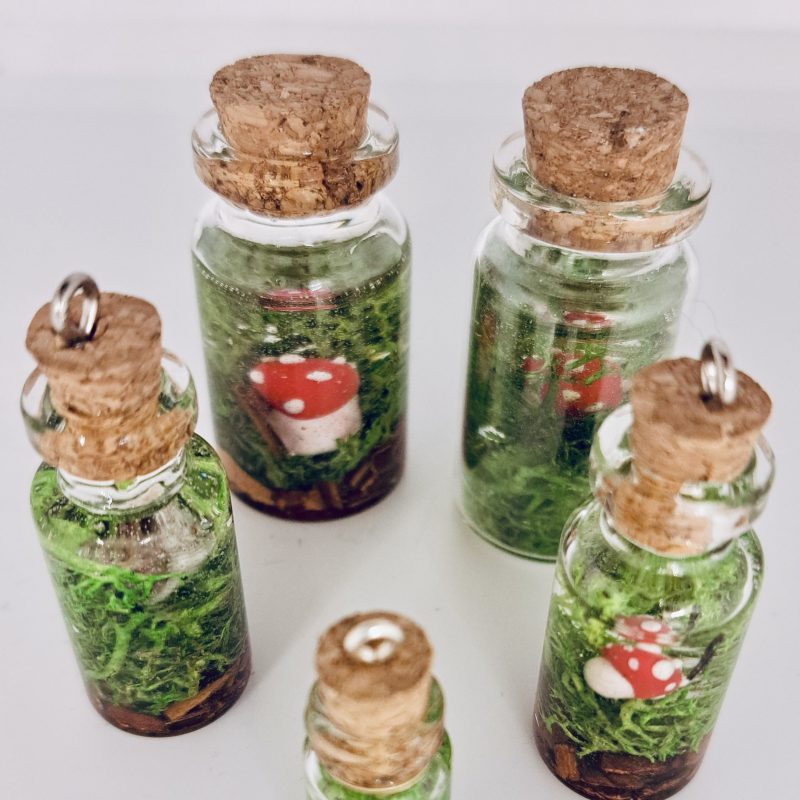 Miniature resin terrariums by Roisin O'Hare. The image shows several small glass bottles with cork stoppers, each containing moss and miniature mushrooms.