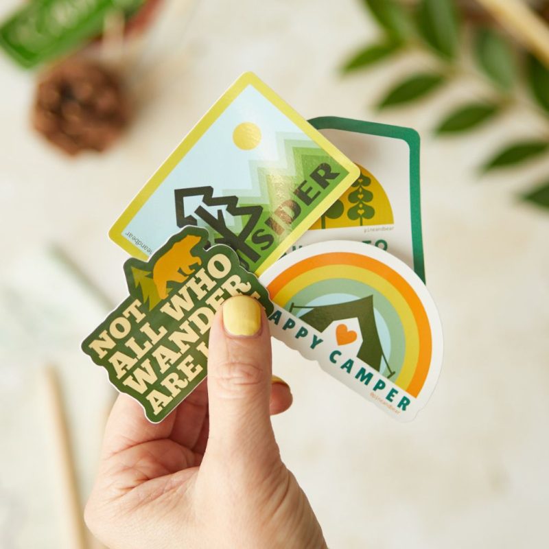 A hand holding 4 outdoor inspired vinyl stickers