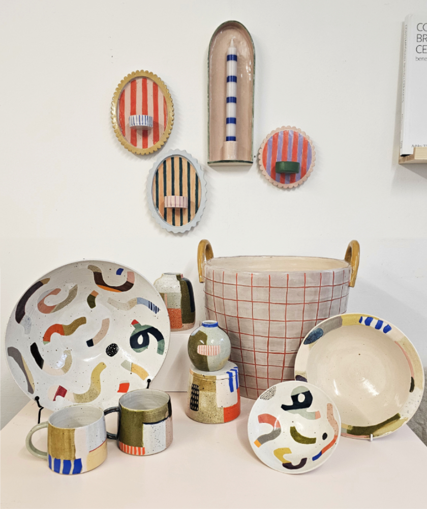 A selection of colourful ceramic pieces are arranged on a table and on the wall behind are a few ceramic sconces.