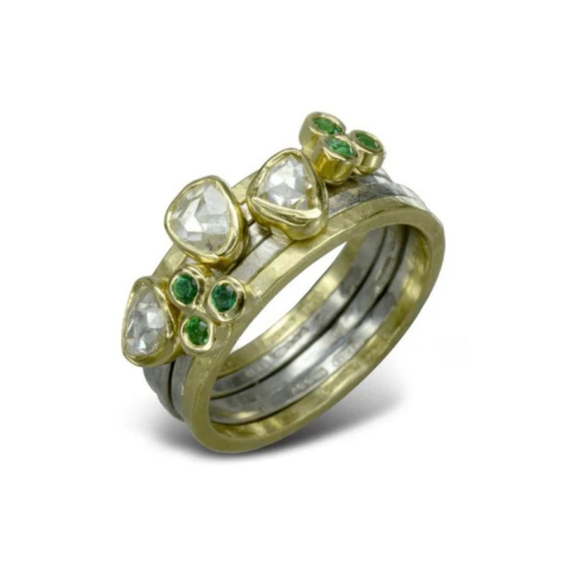 A stacked set of fine hammered gold and silver rings with a rough diamond or set of three small emeralds on each band, set in thin gold surrounds.