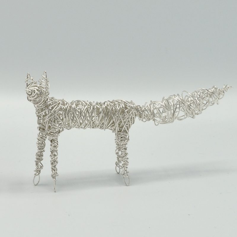  A small wire sculpture of a stylised fox, made with silver plaited wire, thinly woven so that it is see through.