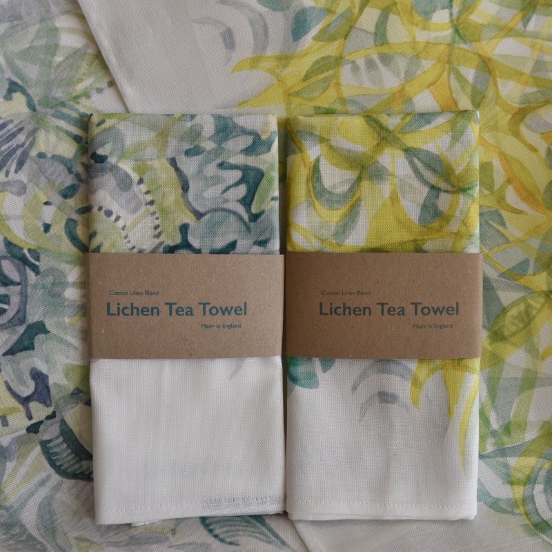 A pair of tea towels printed with lichen watercolour paintings in shades of yellow and green and intricate abstract layers of colour and organic shapes