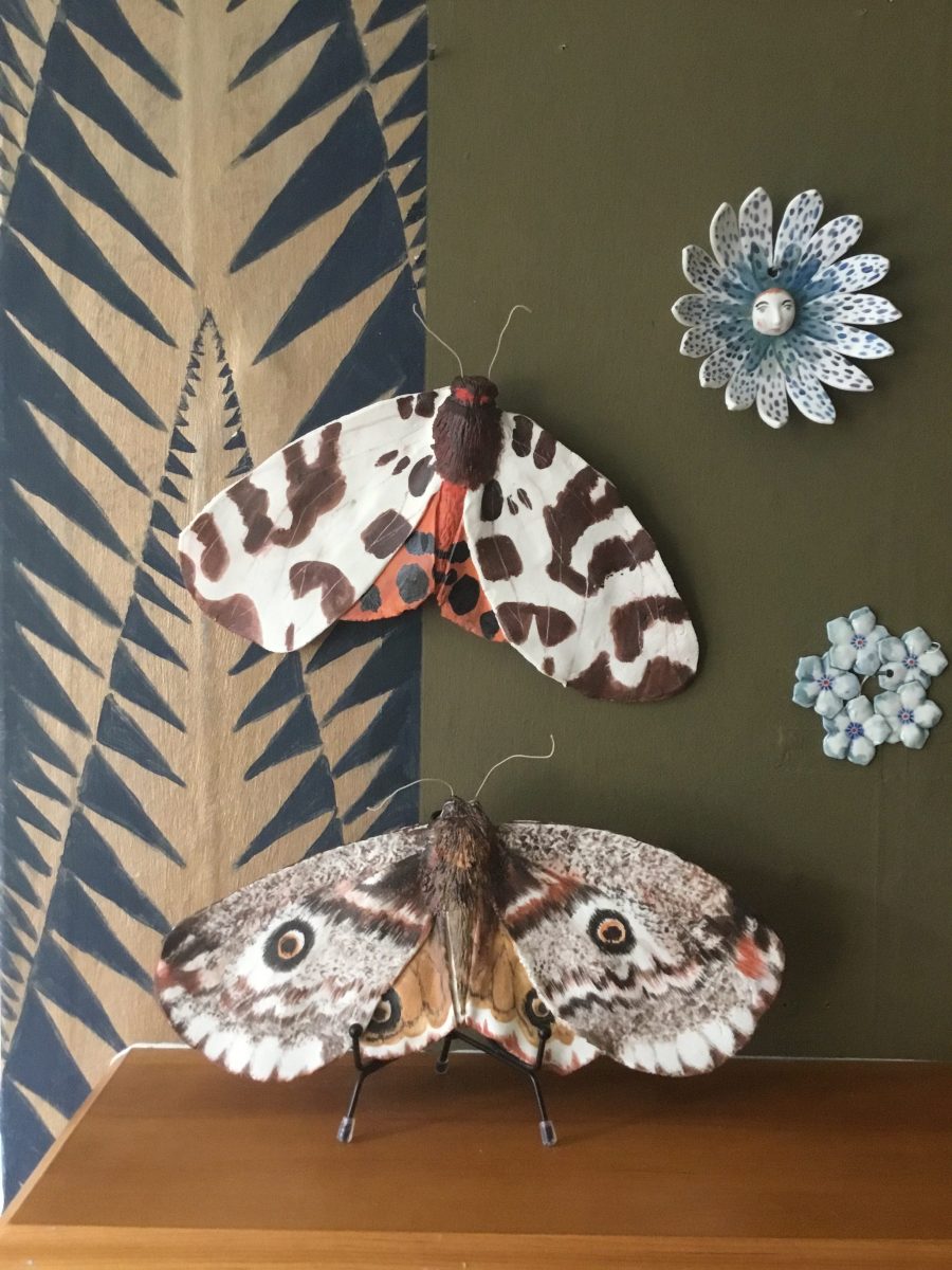 2x Giant ceramic moths handpainted in colours , Matt texture mounted onto the walls with large flower heads .
