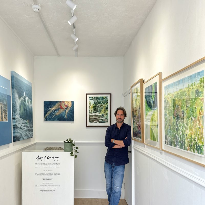 Matt James Brown stood in the Land and Sea Gallery with his landscape paintings on the walls