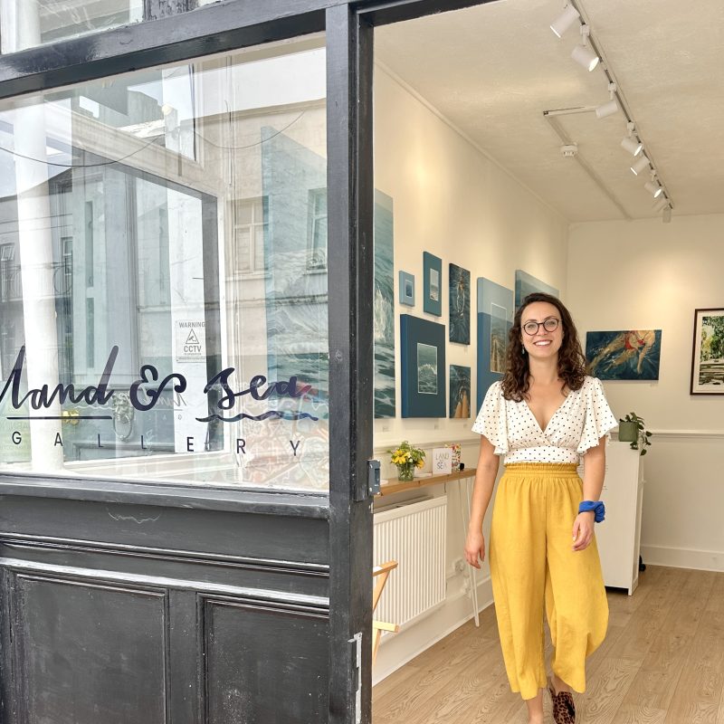 Emma Christopherson stood inside the Land and Sea Gallery with her seascape paintings on the walls