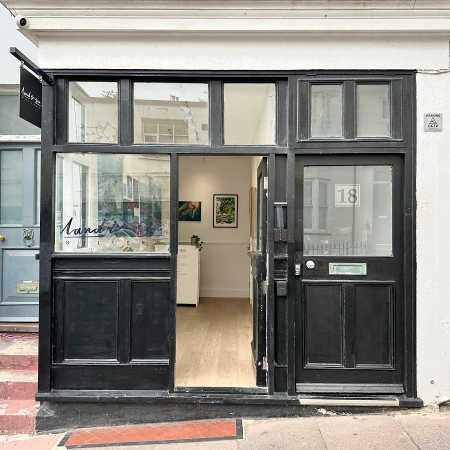 The outside of the Land and Sea Gallery - a black panelled shopfront with windows and paintings on the walls inside