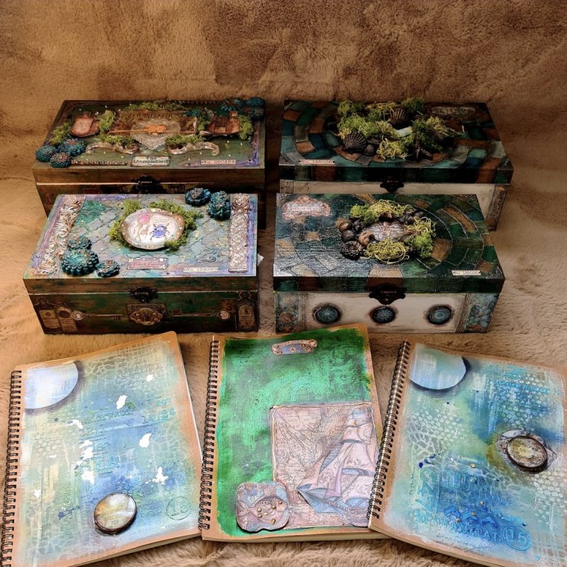 Art boxes and notebooks by the artist Lucy Stearman;  each has intricate mixed-media embellishments, including paint, decoupage, and added elements such as moss, shells, and decorative pieces.