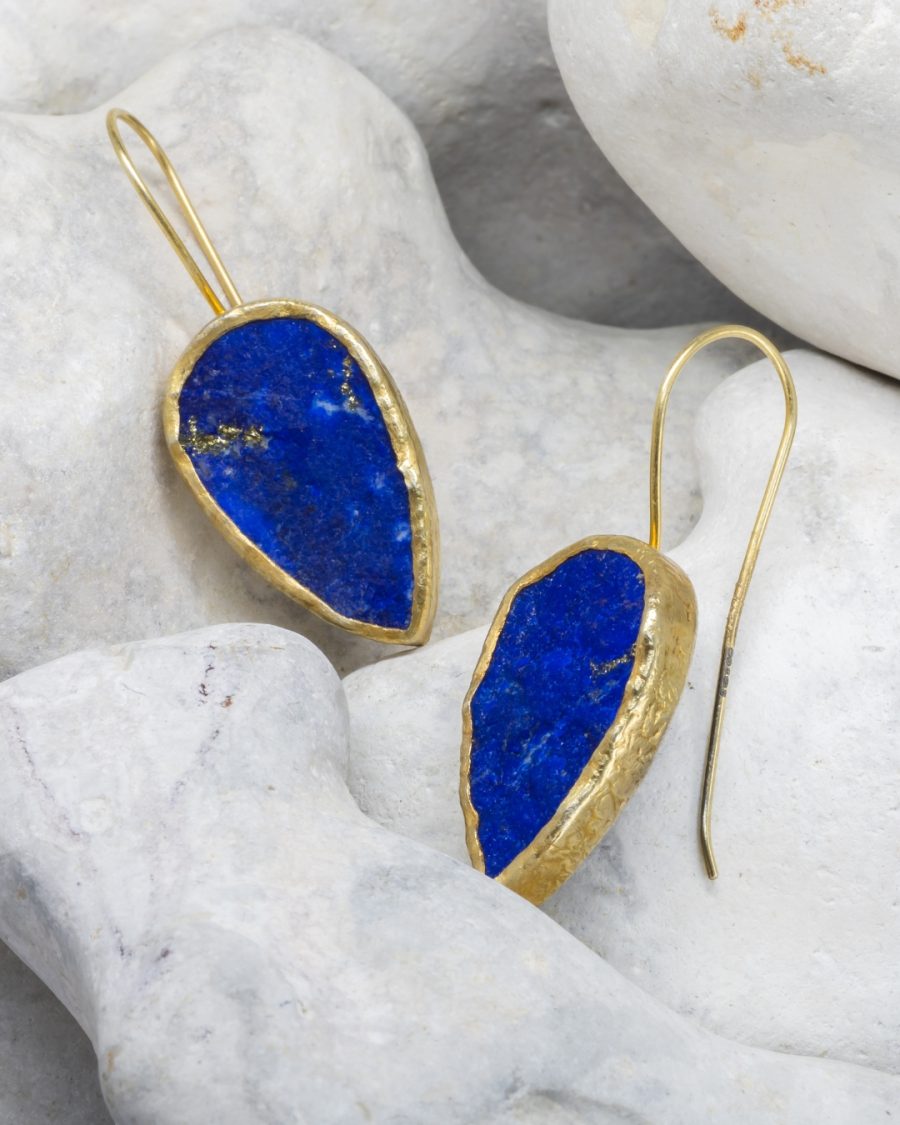 Earrings consisting of upside-down teardrop shaped blue lapis lazuli stones with flecks of gold iron pyrites, set in rough gold surrounds with hook wires attached