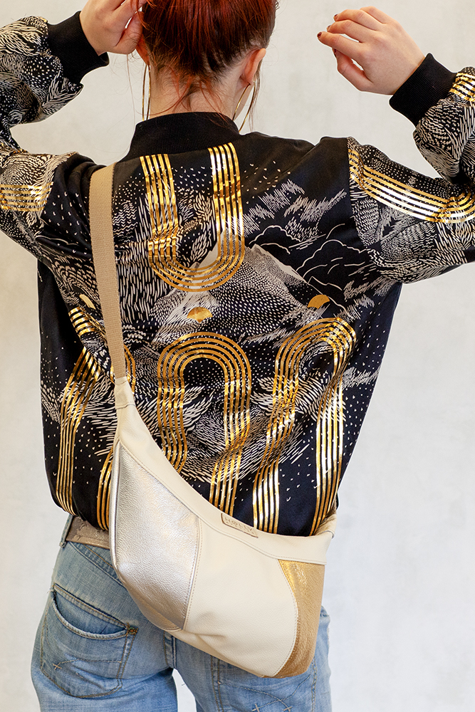 Woman wearing black and gold bomber jacket with metallic leather bag