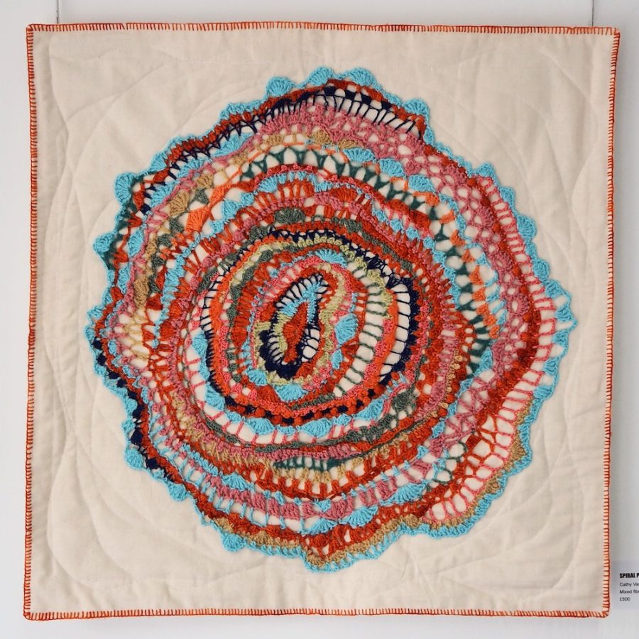 Crochet textile artwork; turquoise, orange, and pink freeform crochet stitches on a quilted canvas backing, edged with hand-stitched border in orange yarn. 