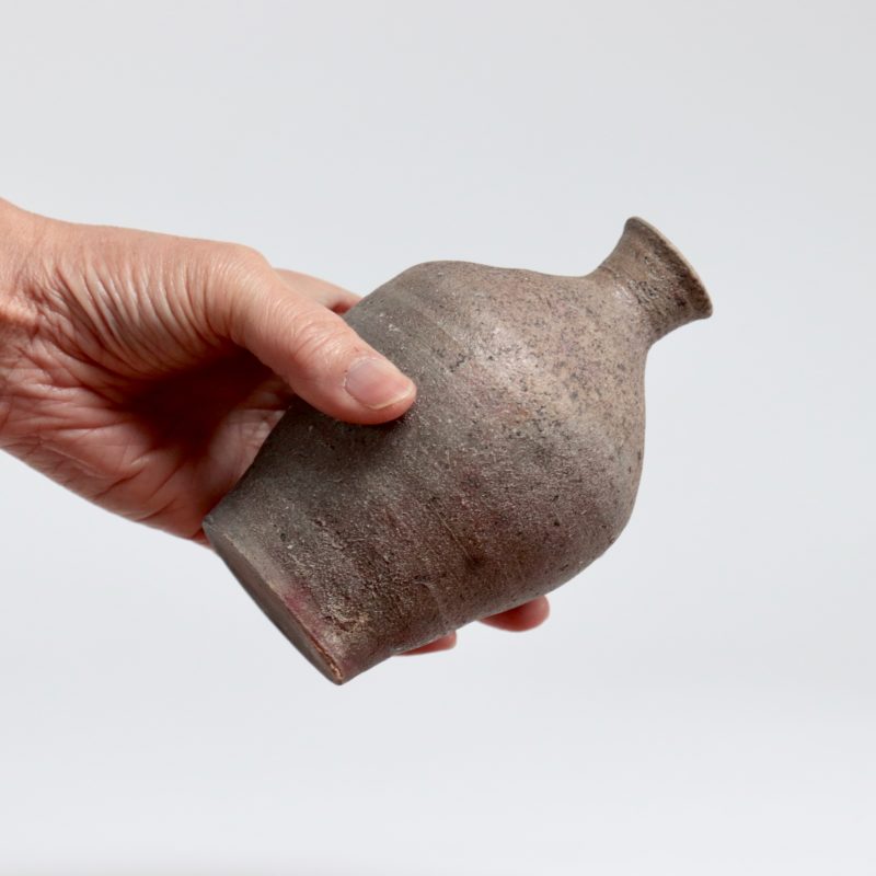 charcoal grey bottle with narrow neck with flower in.