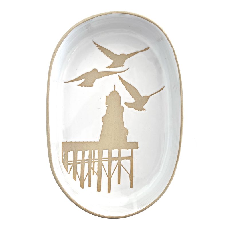 A stoneware server dish with white tin glaze and a stencil motif of the helter skelter on Brighton pier with a starling in the foreground.