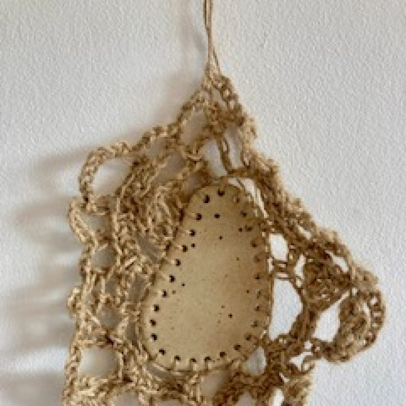 A wall hanging featuring a ceramic piece with embroidery around the edge