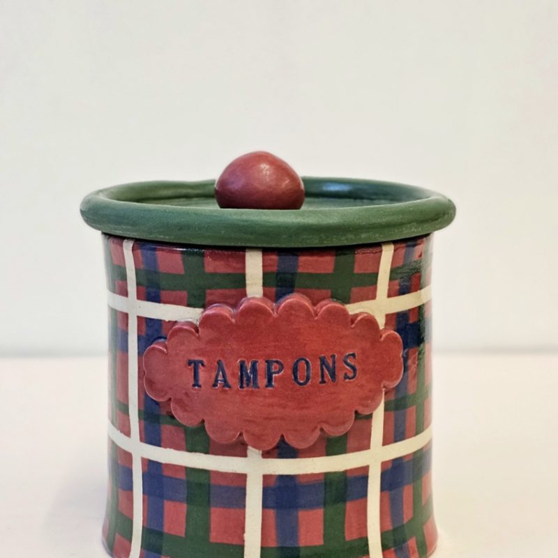 A tartan painted ceramic pot with a label reading Tampons