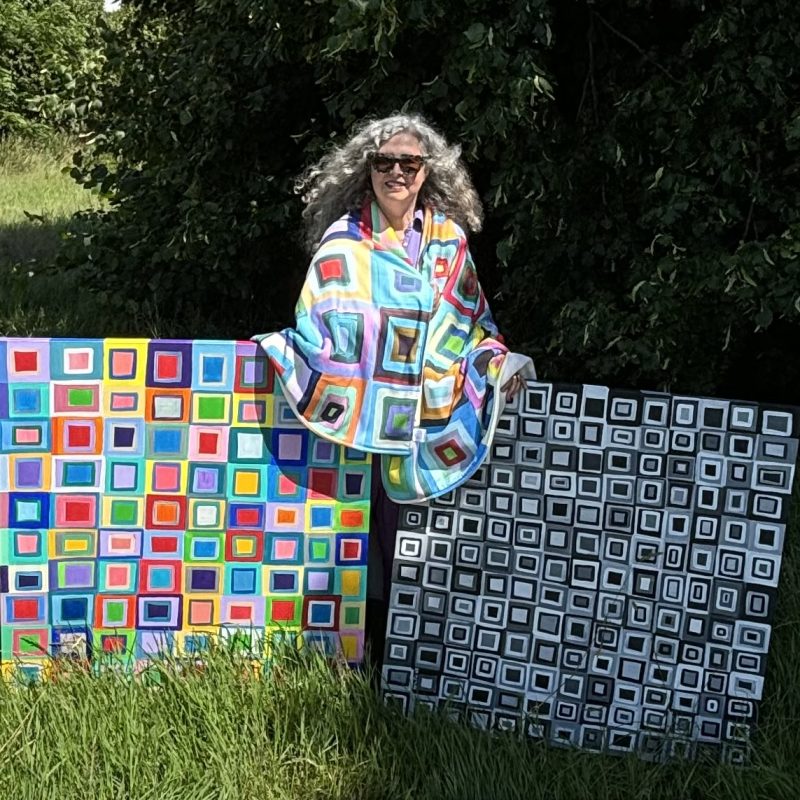 The artist with 2 of her windows painting and a blanket designed in the forest 