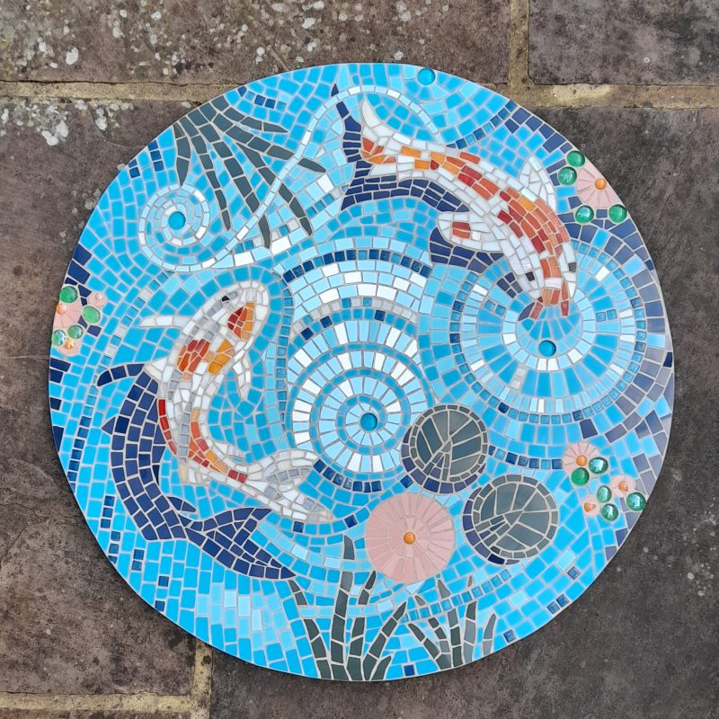 Round mosaic plate depicting koi carp swimming in a pond,  blue background with vibrantly coloured fish