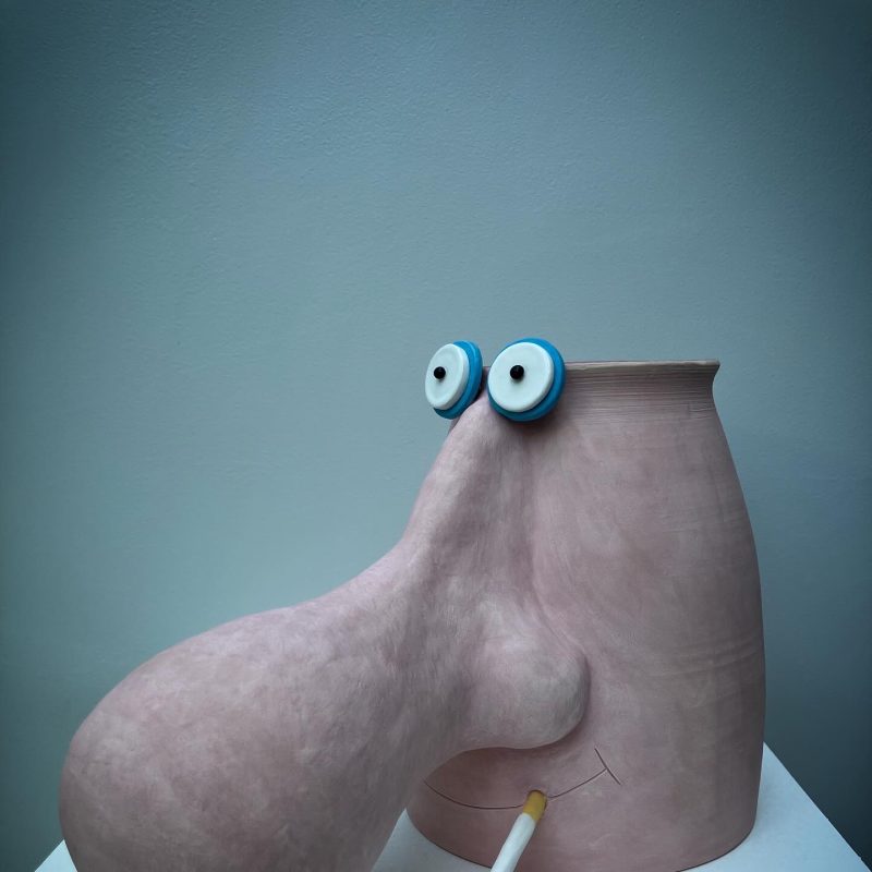 A pastel pink ceramic vase featuring a face with a huge bulbous nose.