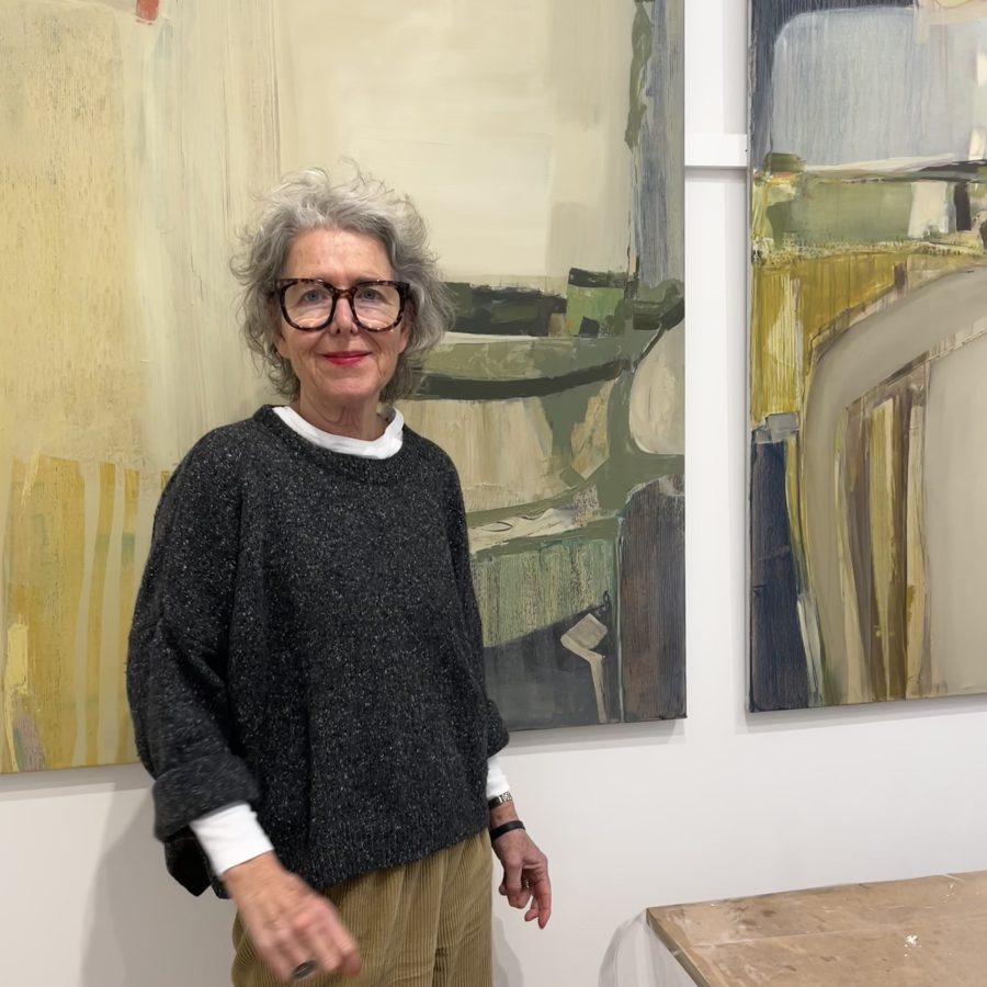 Artist Jo Watters-Pawlowski standing in her studio, in front of two paintings.