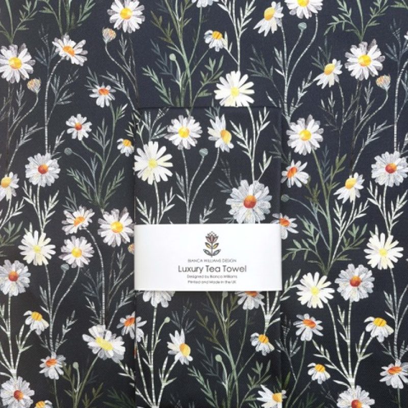 Luxury tea towel designed with yellow centred daisies and white petals on a rich dark background.