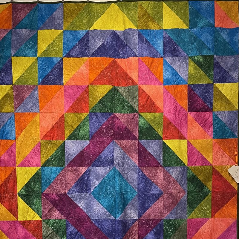 A beautiful quilt made of coloured triangles put together in an overall diamond design