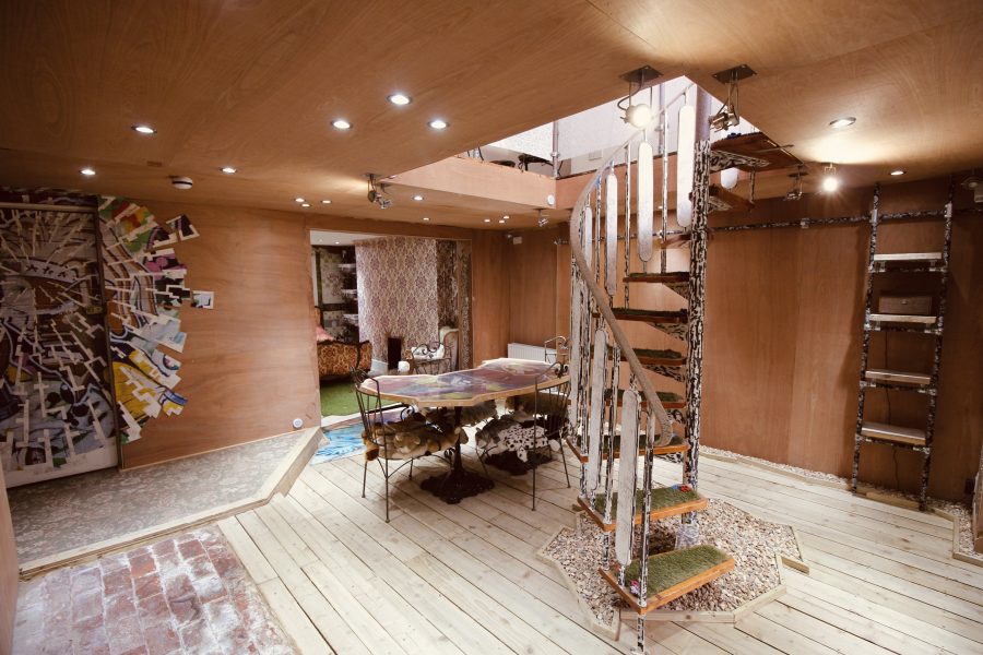 A photo of a bespoke room with a spiral staircase and a colourful graffiti piece in the corner with lots of wall space and a table in the middle of the room where workshops and performance will happen.