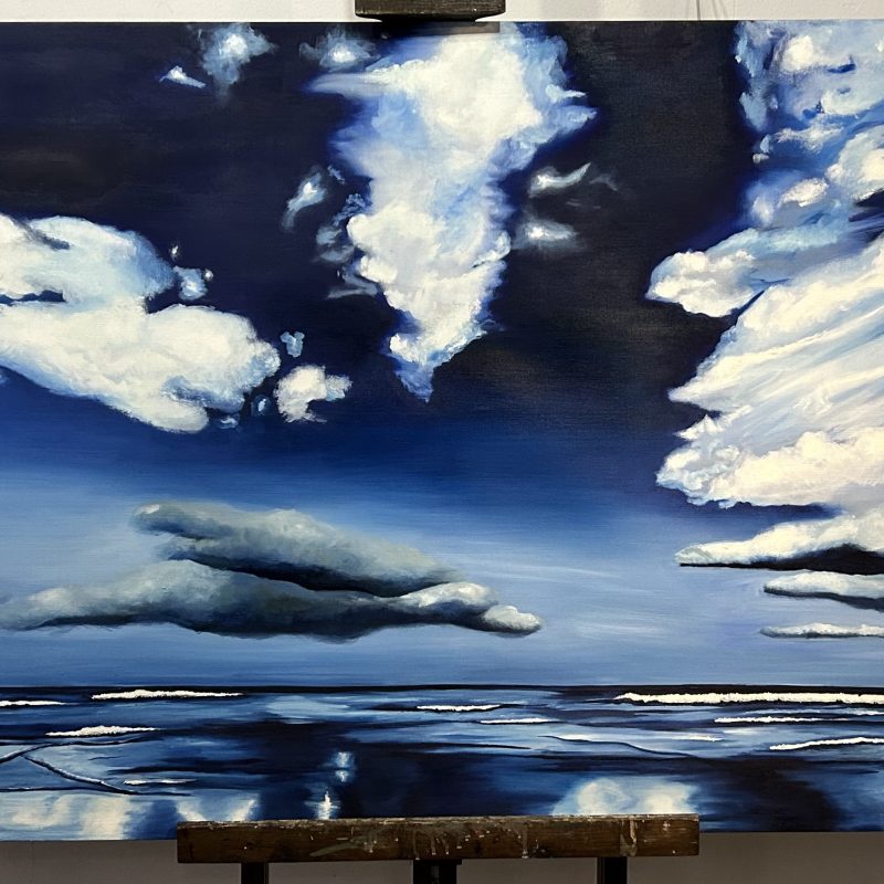 A large blue sky painting with white spralling clouds over a low tide. 