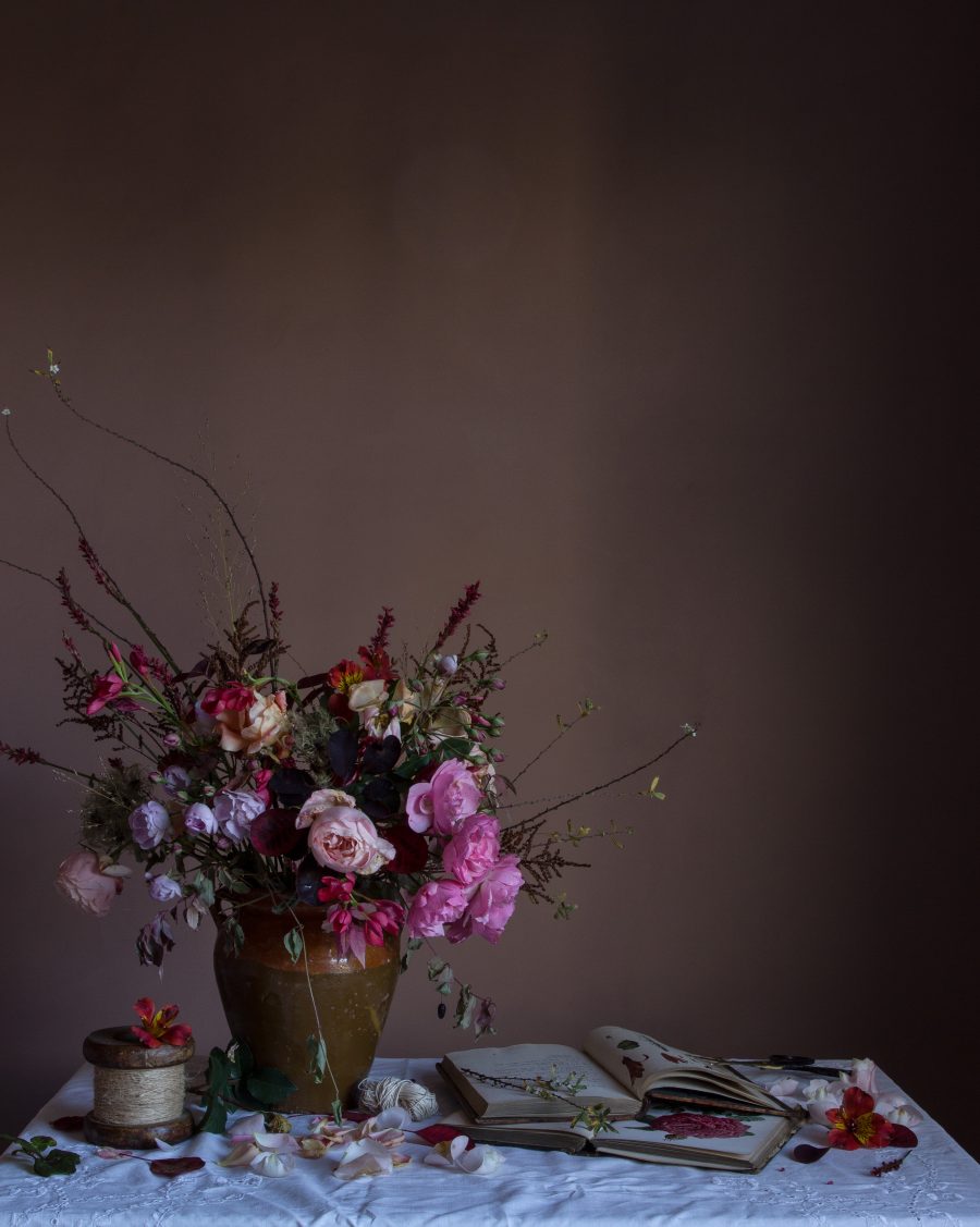 A still-life of roses in a vase alongside old books