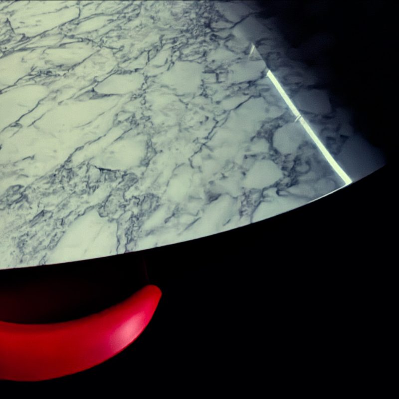 An abstraction of a white marble Eero Saarinen table and a red Verner Panton chair with fragments of sun and shade.