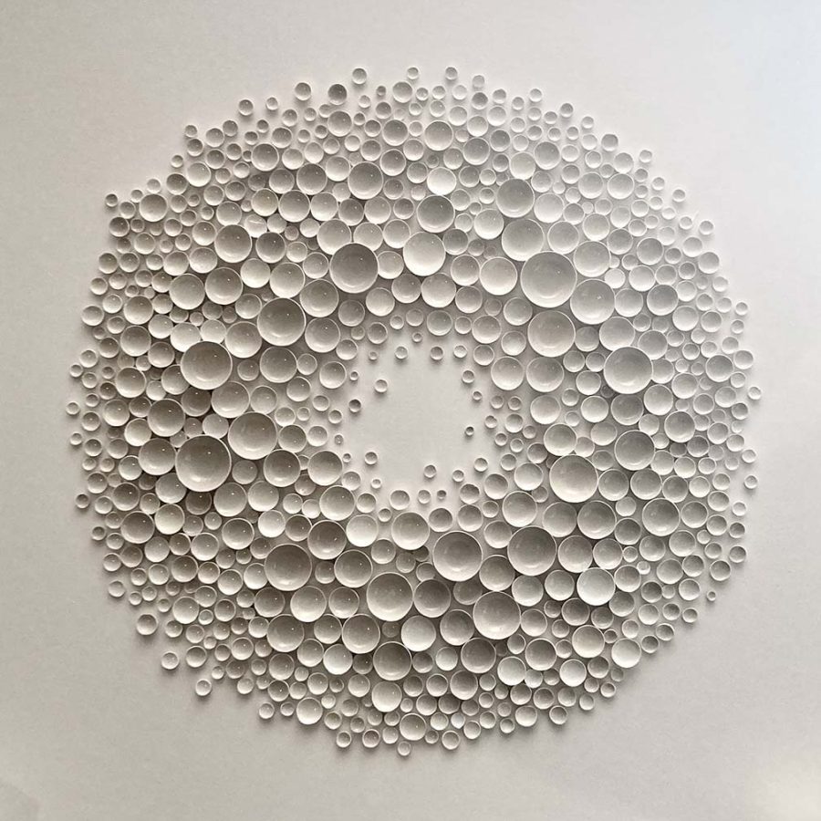 Tiny white glazed clay vessels arranged on a canvas like a fairy ring or sea urchin