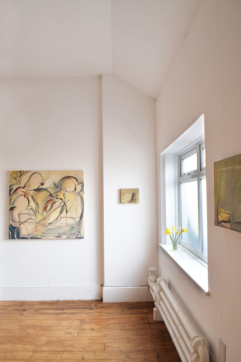 A room in One Church Brighton, with a wooden floor and white walls, has artworks displayed and daffodils on the windowsill.