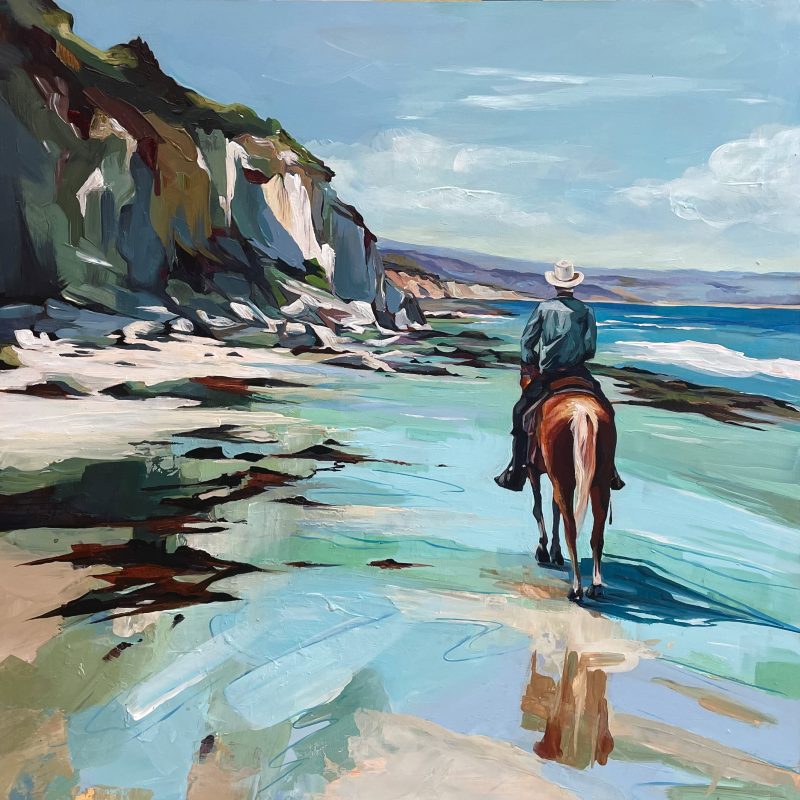 A cow boy rides his horse in the beach with cliffs to the side