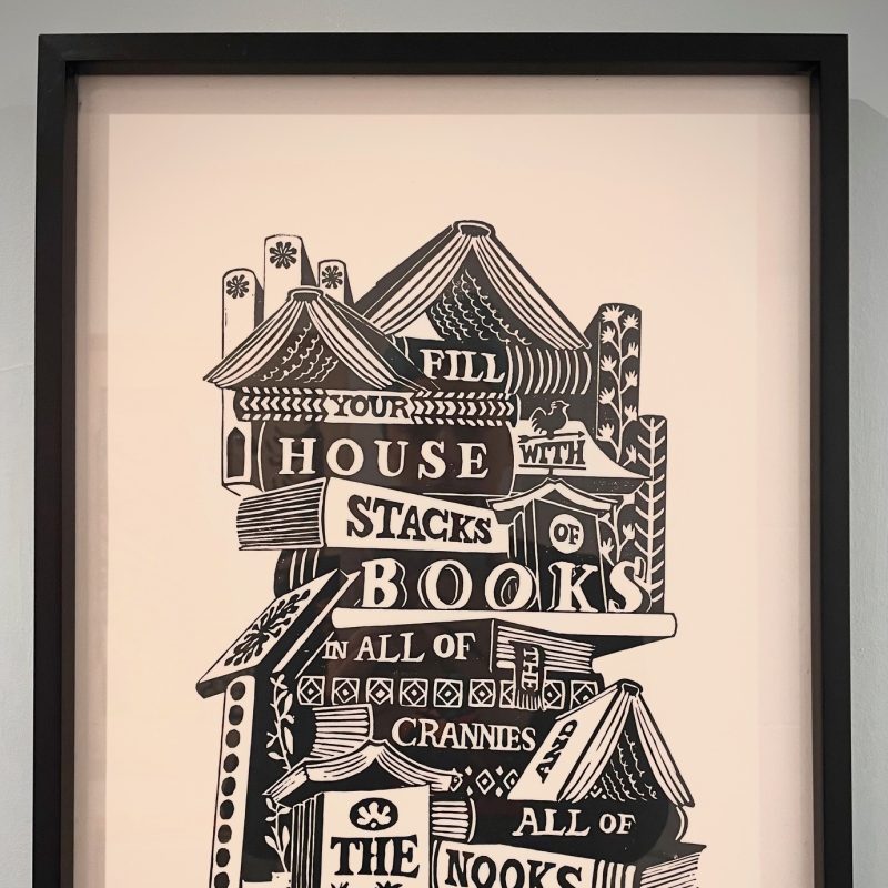 Black and white Lino cut with image with a stack of books with written words